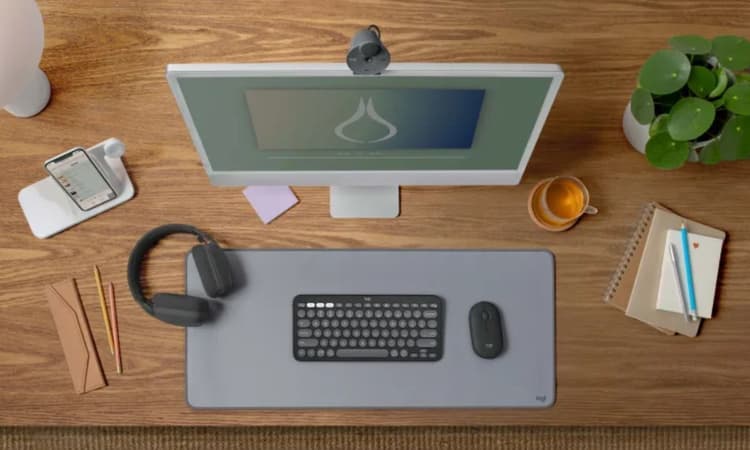 簡約木質桌面上的羅技鍵盤與滑鼠,搭配電腦螢幕、耳機與文具。