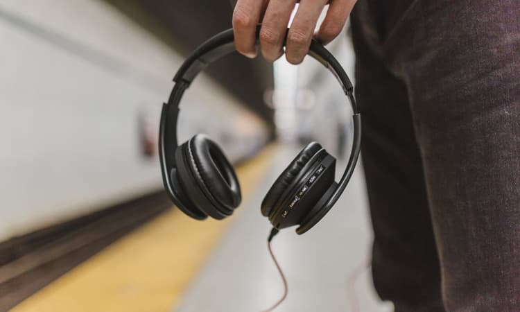 一個人手持黑色有線耳罩式耳機,站在地鐵月台上。