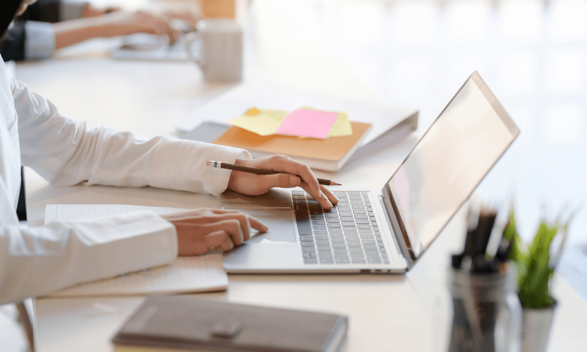 辦公室環境中,穿著白襯衫的人使用輕薄筆電,一邊打字一邊做筆記。