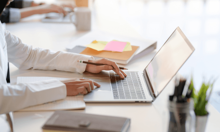辦公室環境中,穿著白襯衫的人使用輕薄筆電,一邊打字一邊做筆記。