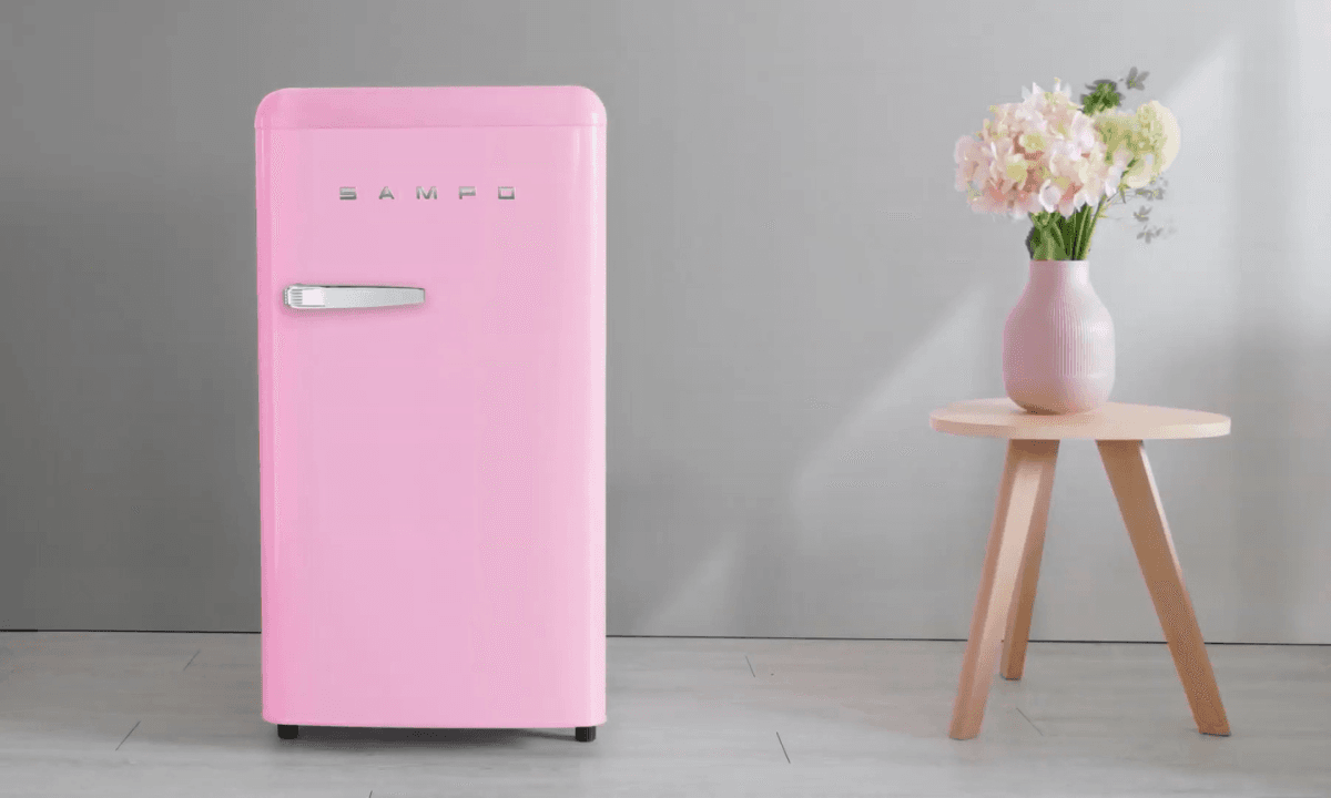 粉紅色聲寶冰箱擺放在簡約現代風格的室內空間,旁邊有一張木質小圓桌與粉色花瓶插花