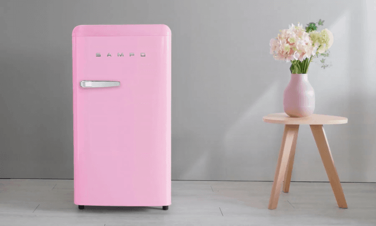 粉紅色聲寶冰箱擺放在簡約現代風格的室內空間,旁邊有一張木質小圓桌與粉色花瓶插花