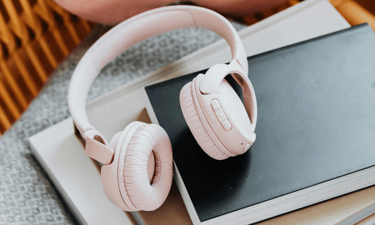 5 款降噪耳機推薦,音質、續航、舒適度全面分析!淺粉色耳罩式降噪耳機放在書本上,展現柔和簡約的質感設計。