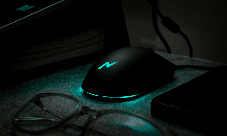 黑色電競滑鼠,旁邊放著眼鏡、電腦和手機