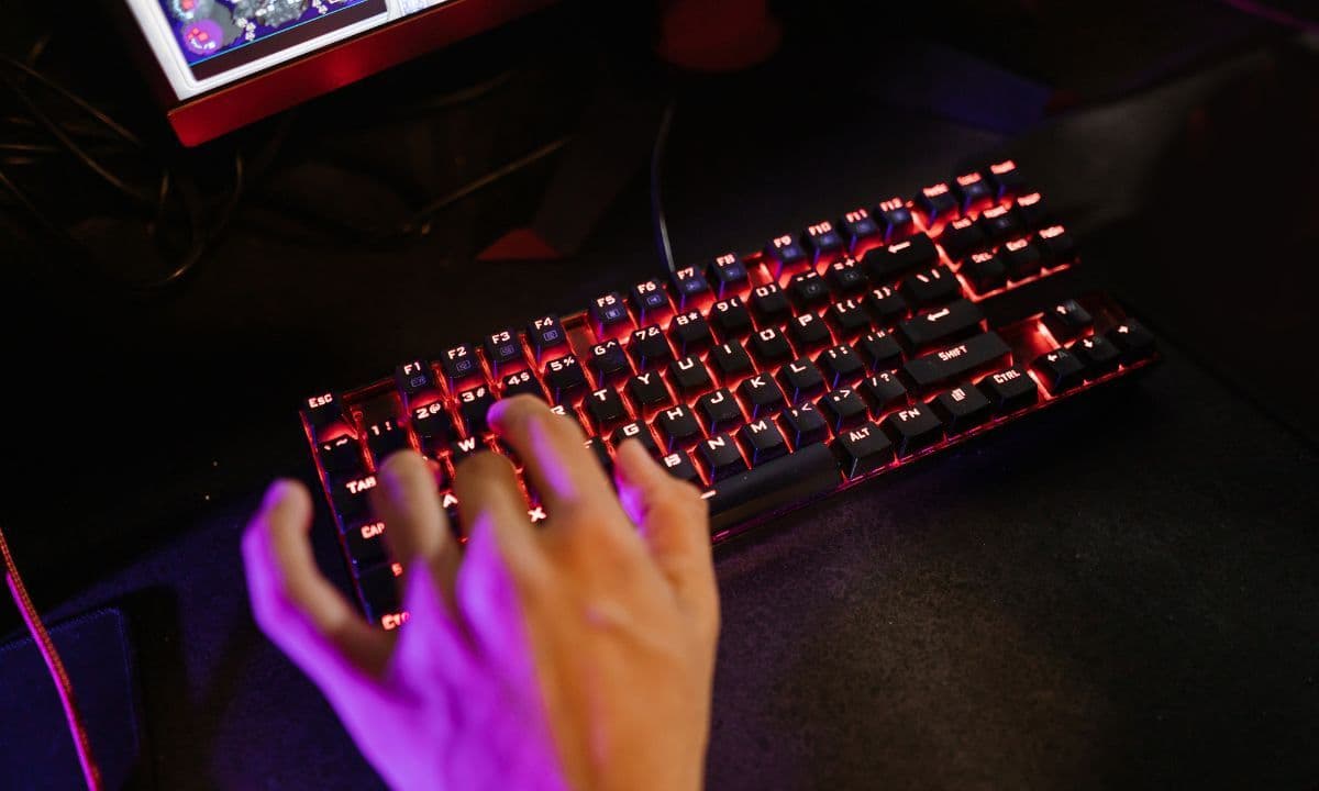 玩家使用紅色背光的電競鍵盤,手部快速操作,螢幕上正在進行遊戲畫面。
